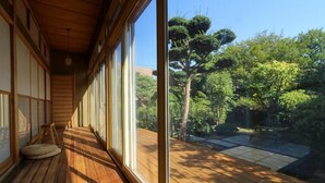 Una habitación japonesa tradicional con suelo de tatami, puertas correderas y vistas a un jardín con árboles y un sendero de piedra.