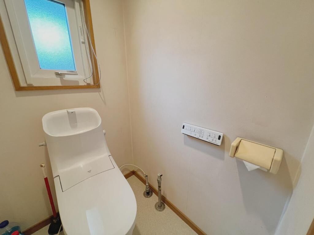 A small bathroom with a toilet, a window, a power outlet, and a hand dryer.
