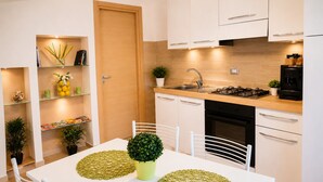 A modern kitchen with white cabinets, a stove, sink, and a dining table with chairs. - The Sisters a stone's throw from Taormina (Santa Teresa di Riva)