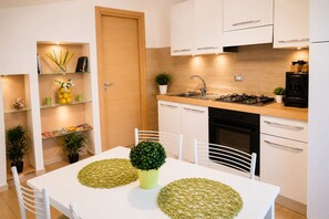 Una cucina moderna con mobili bianchi, un fornello, un lavandino e un tavolo da pranzo con sedie.