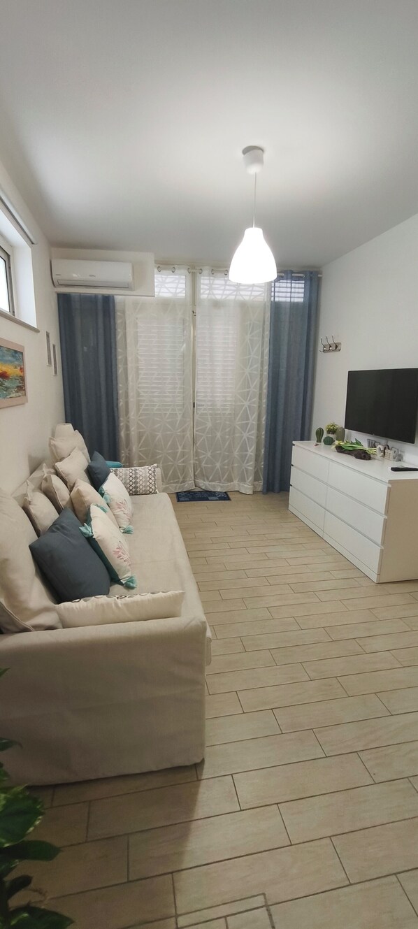 A living room with a sofa, a TV, a white dresser, and a ceiling fan.