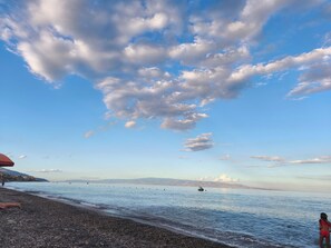 A pebbled beach with calm water, a clear sky, and distant mountains.