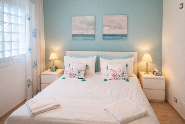 A bedroom with a bed, two nightstands, lamps, a window with curtains, and two wall art pieces.