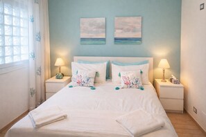 A bedroom with a bed, two nightstands, lamps, a window with curtains, and two wall art pieces.