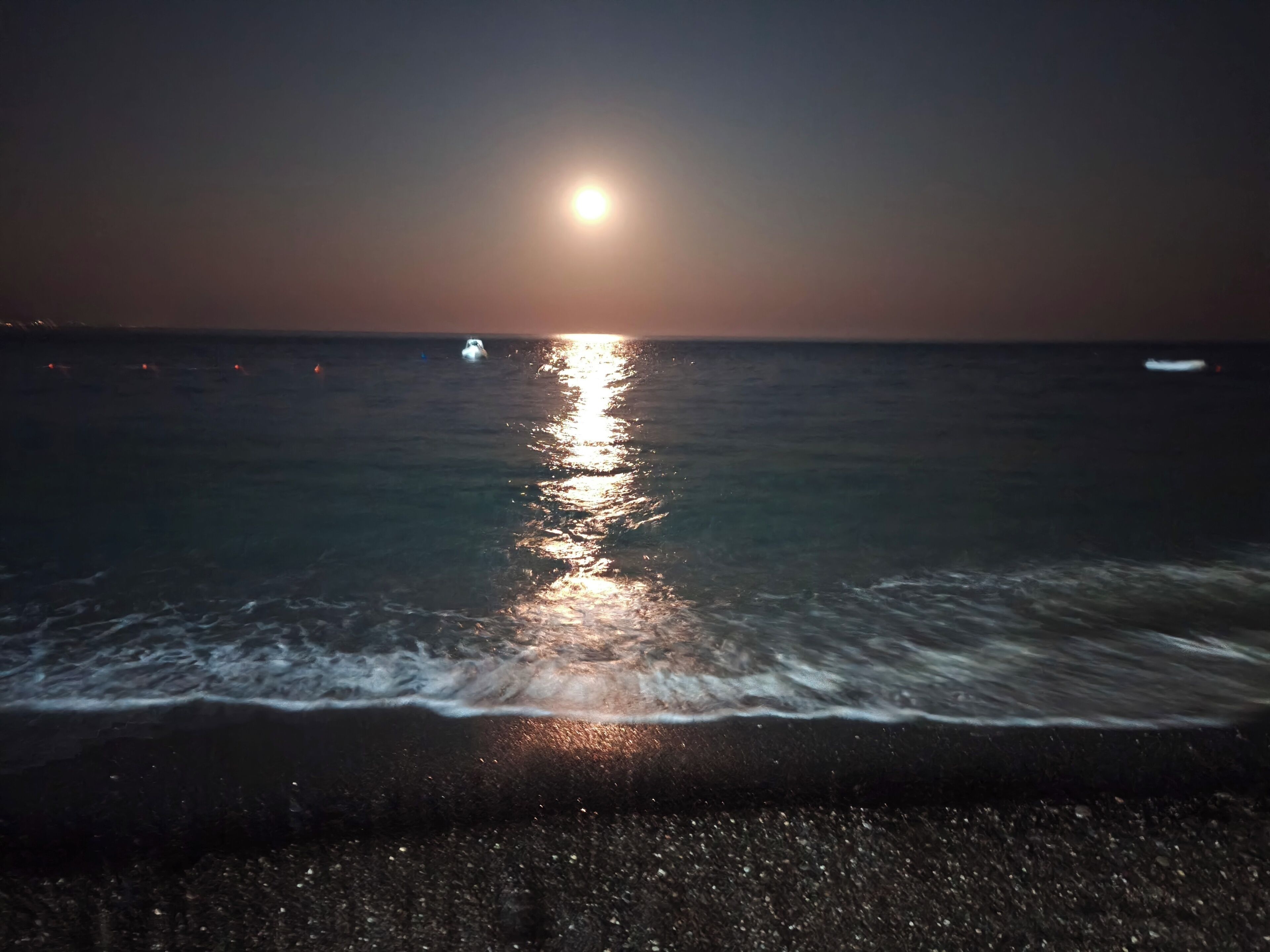 Une plage de nuit, avec un bateau visible sur l’eau.