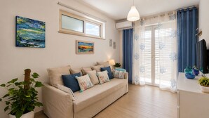 A living room with a sofa, a cat tree, a painting, and a window with curtains. - The Sisters a stone's throw from Taormina (Santa Teresa di Riva)