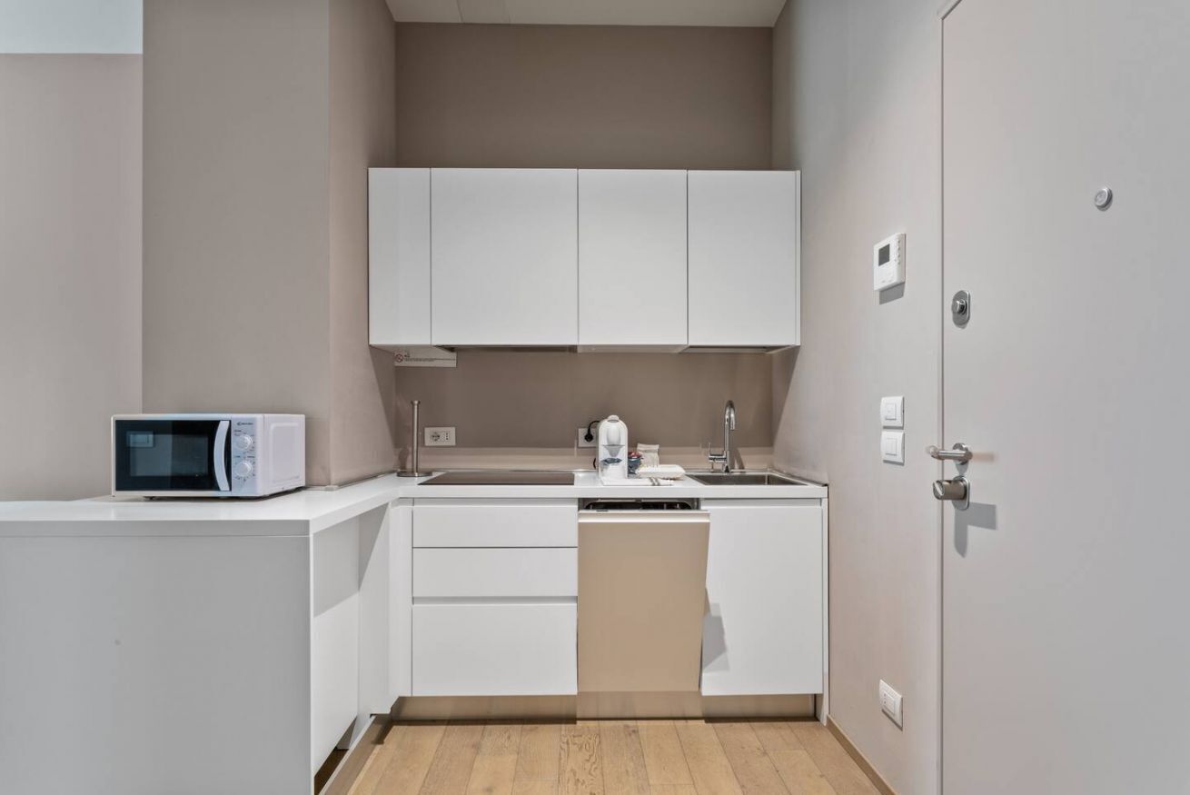 A compact kitchen with white cabinets, a microwave, a coffee maker, and a dishwasher.