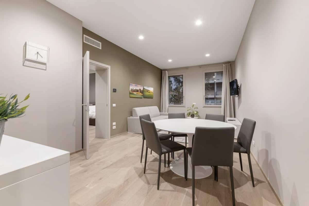 A modern dining area with a round table and six chairs, a whiteboard, and a clock on the wall.