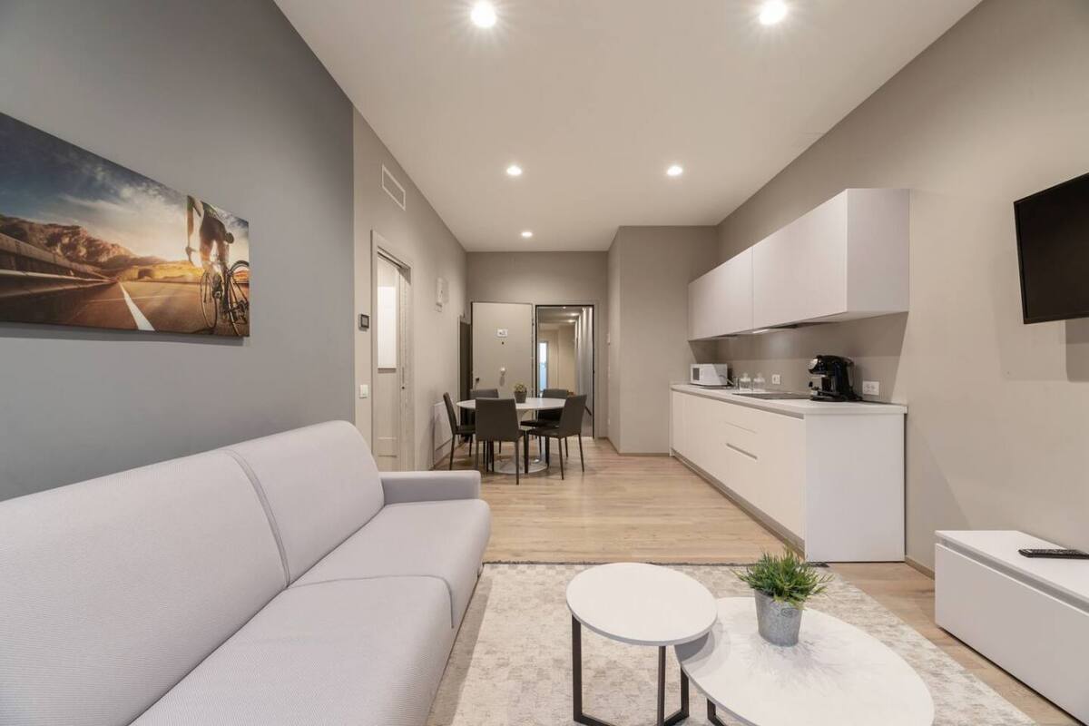A modern living room with a sofa, a dining area with chairs, and a kitchen with cabinets and appliances.