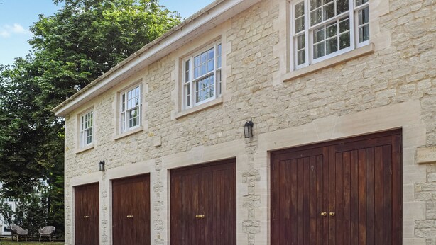 A stone building with four large wooden garage doors and a gravel driveway. - 1 bedroom accommodation in Tetsworth, near Oxford (Tetsworth, near Oxford)