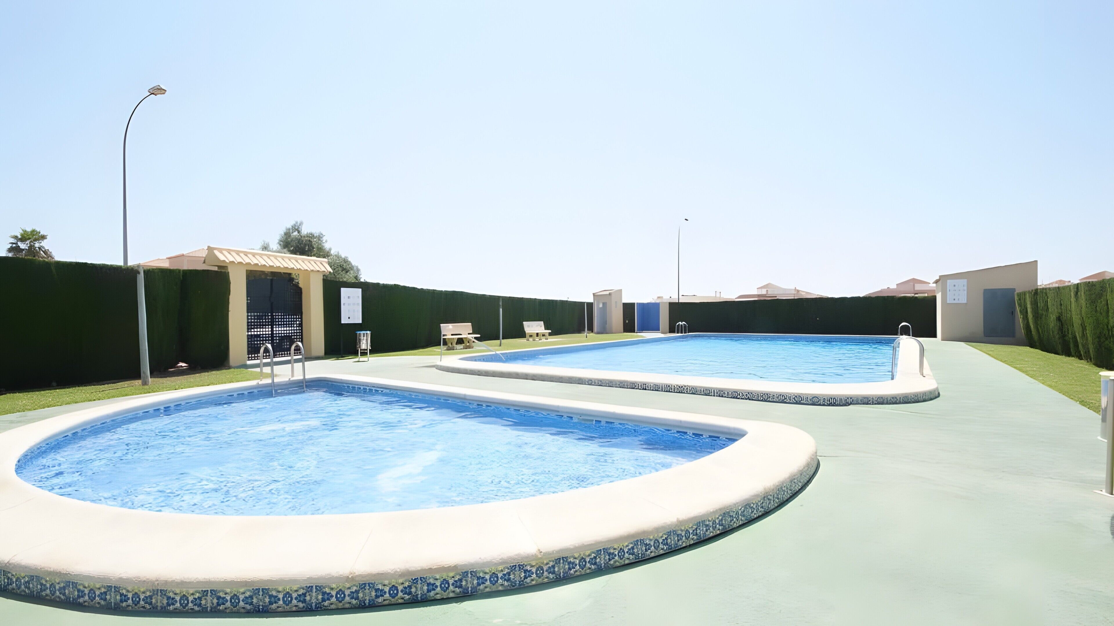 Deux piscines rectangulaires bordées de carreaux, entourées d’une allée pavée, et un petit bâtiment avec une porte et une fenêtre sur le côté gauche.