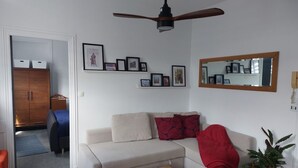 A living room with a sofa, a coffee table, a ceiling fan, framed pictures on the wall, and a mirror. - Apartment for 2 people in the heart of downtown Epernay- Champagne, (Epernay)