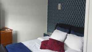 A neatly made bed with white and blue bedding, a red patterned pillow, and a ceiling fan. - Apartment for 2 people in the heart of downtown Epernay- Champagne, (Epernay)
