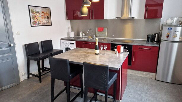 A modern kitchen with red cabinets, a stainless steel refrigerator, a built-in oven, and a dining area with a table and chairs. - Apartment for 2 people in the heart of downtown Epernay- Champagne, (Epernay)