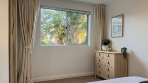Quarto com cama, penteadeira, janela com cortinas e quadro na parede.