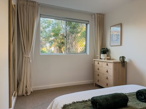 A bedroom with a bed, a dresser, a window with curtains, and a framed picture on the wall.