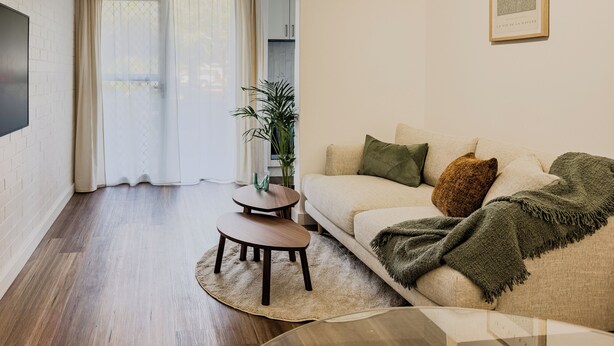 Uma sala de estar moderna com um sofá, uma mesa de centro e uma TV fixada na parede.