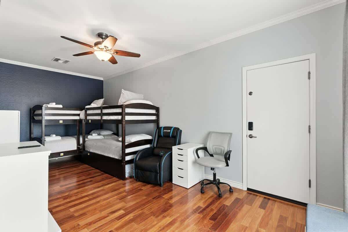 A room with bunk beds, a desk, a chair, a ceiling fan, and a door.