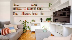 Een woonkamer met een grijze bank, een witte salontafel, een televisie en een boekenkast vol boeken.