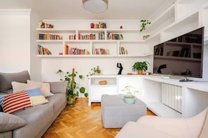 A living room with a grey sofa, a white coffee table, a TV, and a bookshelf filled with books.