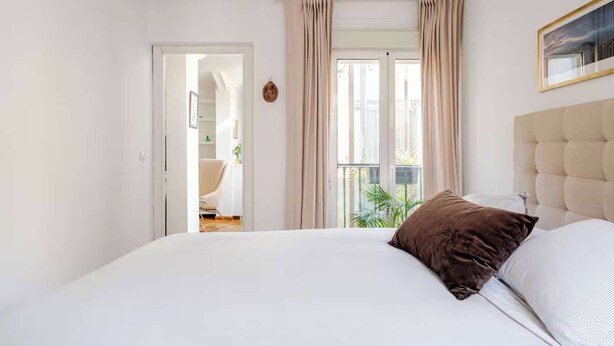 Een slaapkamer met een bed, gordijnen, een raam en uitzicht op de omgeving.