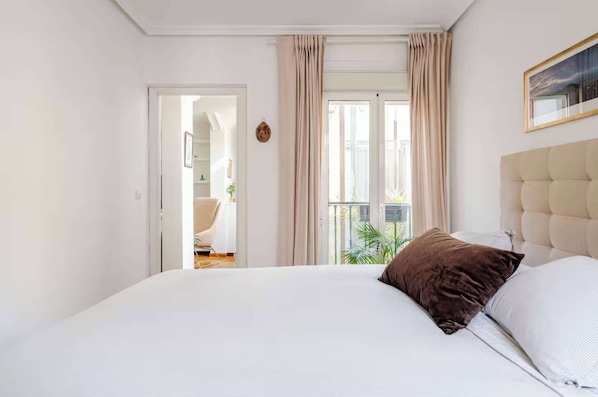 A bedroom with a bed, curtains, a window, and a view of the outdoors.