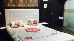 Een slaapkamer met een gebonden hoofdbord, beddengoed met een patroon en een donkerhouten garderobe.