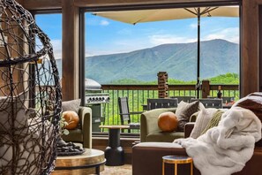 Un espace extérieur accueillant, avec des sièges confortables, une vue sur les montagnes, un fauteuil suspendu et un barbecue.