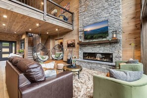 A cozy living room with a stone fireplace, leather sofas, and a hanging chair.
