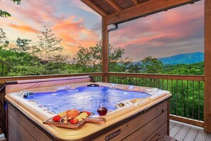 A hot tub with a wooden deck and a scenic view of mountains and trees.