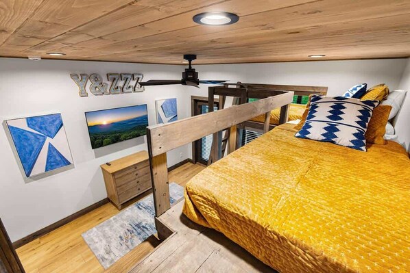 A bedroom with a bed, a ceiling fan, a wooden desk, and artwork on the walls.