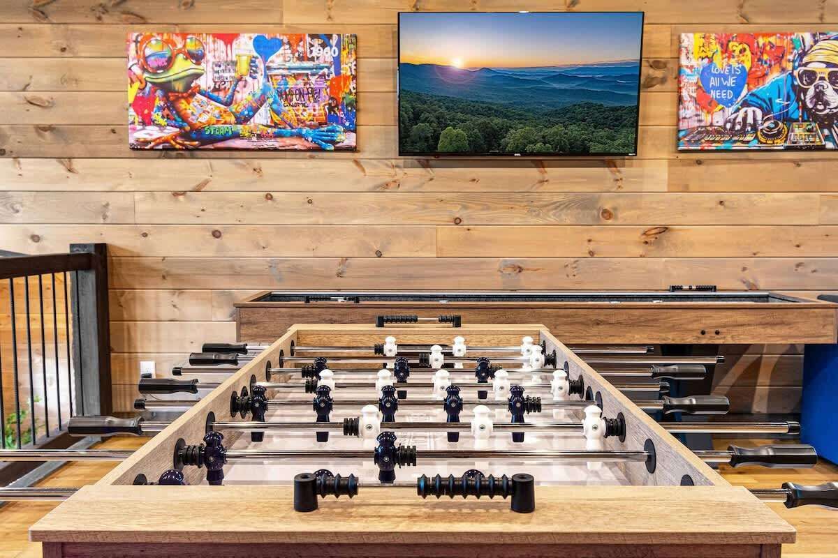 A foosball table in a room with wooden walls and three paintings above it.