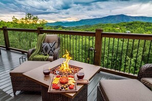 Une terrasse dotée d’un foyer, de meubles en osier et offrant une vue sur les montagnes.