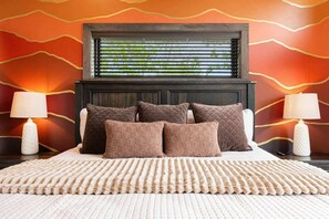 Un lit avec une tête de lit sombre, de nombreux oreillers et un tapis à motifs.