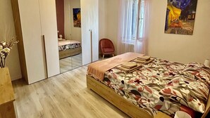 A bedroom with a bed, a chair, a bedside table, a mirror, and a painting on the wall.