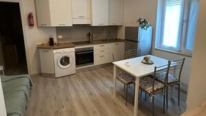 A compact kitchen with a washing machine, a dining table with chairs, and a window with curtains.