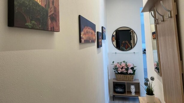 A hallway with a painting of a castle, a mirror, and a small shelf with a basket of flowers.