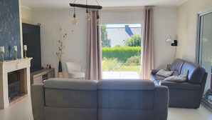 Una sala de estar moderna con un sofá gris, un sofá de cuero marrón, una chimenea y vistas al exterior con vegetación.