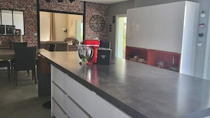 Una cocina moderna con una isla grande, un robot de cocina rojo y vista al jardín a través de la puerta de vidrio.