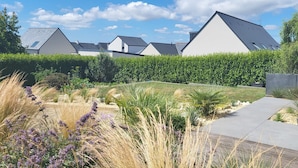 Un barrio residencial con casas modernas, un jardín bien cuidado con diversas plantas y un sendero pavimentado.