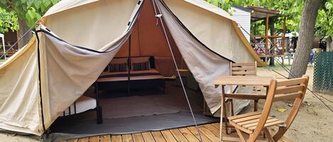 A tent with a bed inside, a table, and a chair outside.