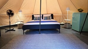 Una habitación con carpa, una cama, un ventilador, una lámpara y un refrigerador.