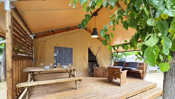 A wooden deck with a table and benches, a hanging light fixture, and a tent structure.