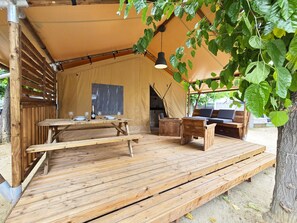 Een houten terras met een tafel en banken, een hanglamp en een tentstructuur.