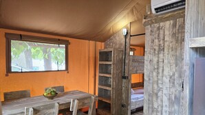 A cozy room with a wooden table, chairs, a window with a view of trees, a ladder, and a bed.