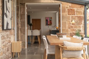 A modern dining area with a wooden table and chairs, stone walls, and a view into the kitchen.