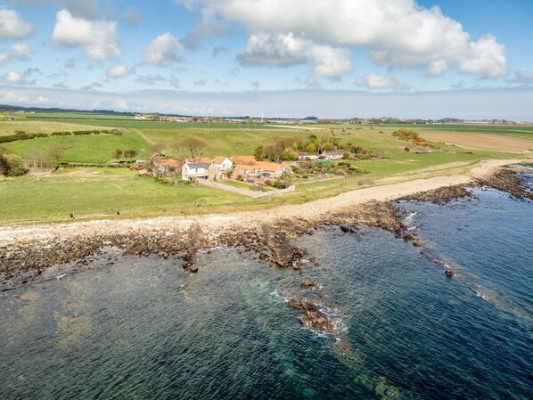 A coastal property with a stone wall, grassy fields, and a clear view of the sea.