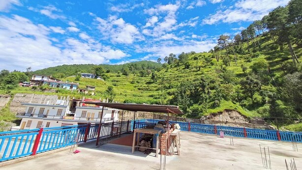 A terrace with a blue railing, a covered seating area, and a view of a hillside with buildings. - Hotel Mountain Paradise Barkot (Barkot)