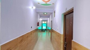 A hallway with a wooden floor, white walls, and a green and orange ceiling. - Hotel Mountain Paradise Barkot (Barkot)