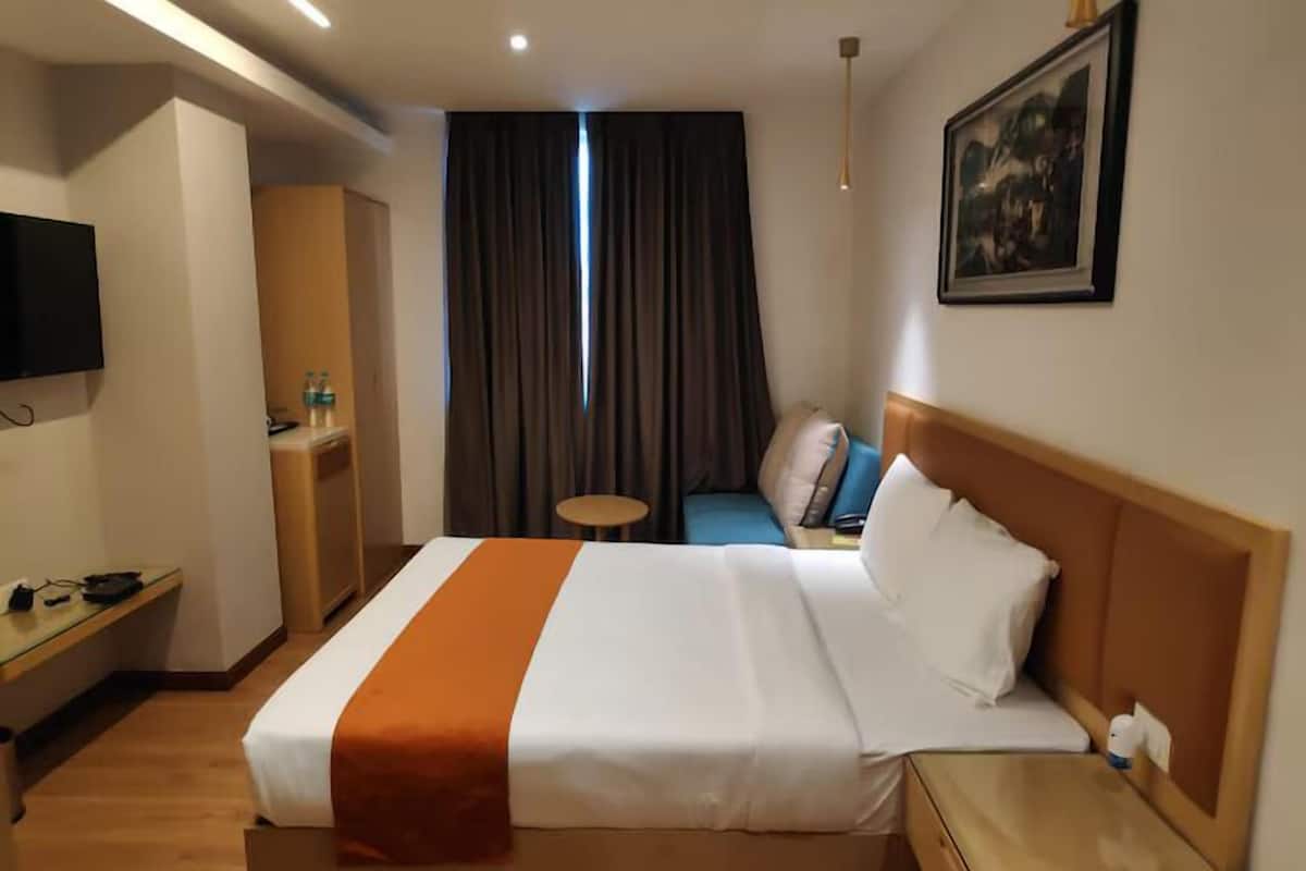 Habitación de hotel con cama, escritorio, silla, mesita, televisor y un cuadro en la pared.